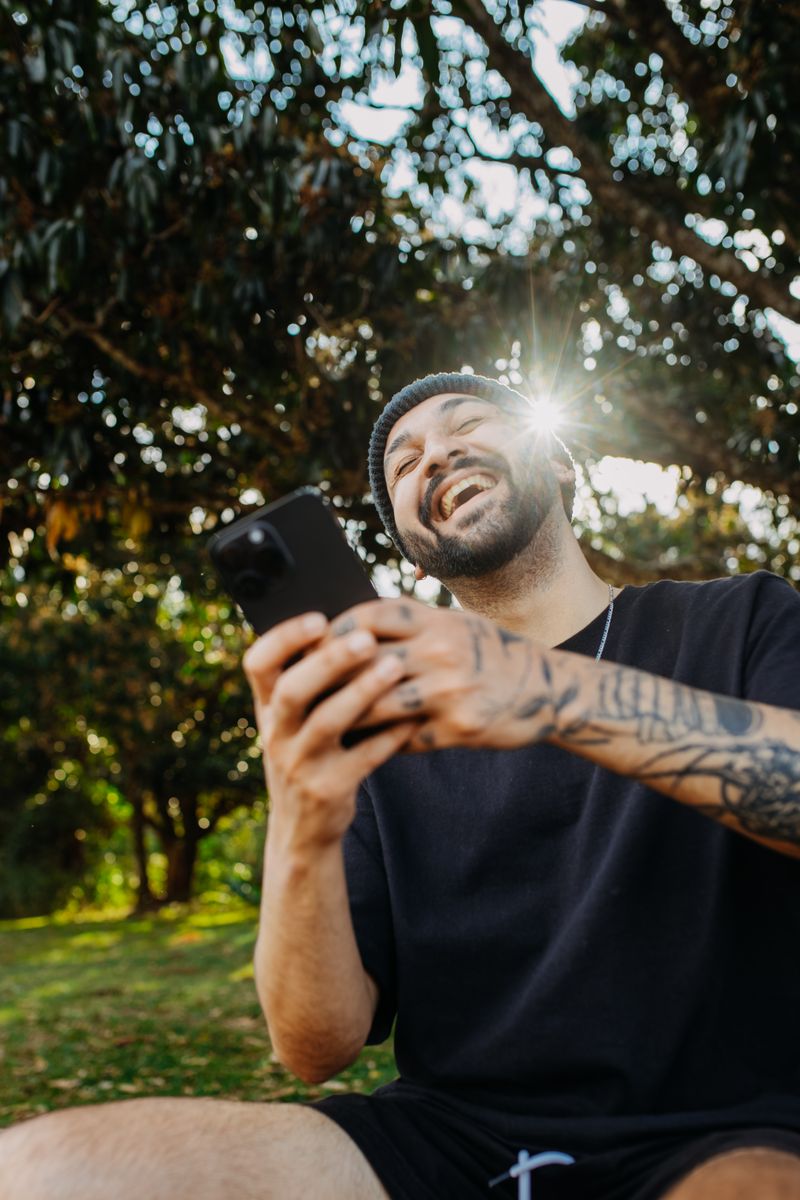 A man laughing at something on his phone in the sun