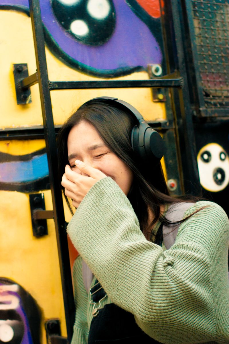 A woman laughing in headphones in front of a painted wall